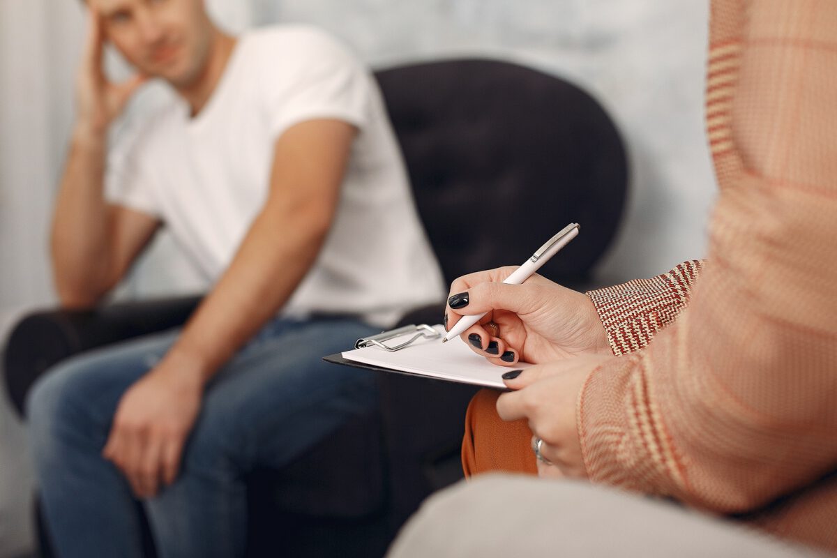 Mężczyzna siedzący na kanapie. Obok psychoterapeutka. W gabinecie odbywa się sesja psychoanalityczna